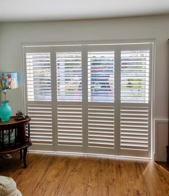 White tracked shutters across a wide patio door in a neutral living room