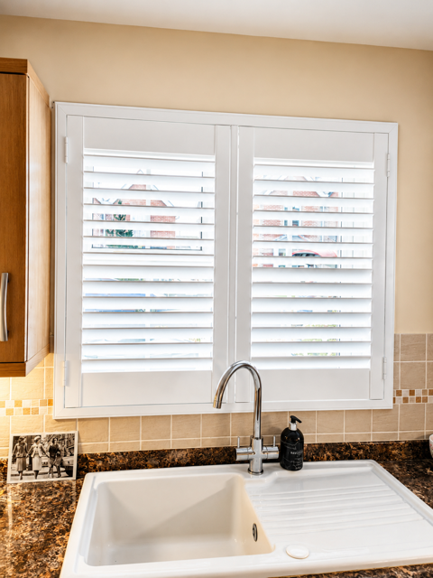 White plantation shutters in a bright kitchen window above the sink