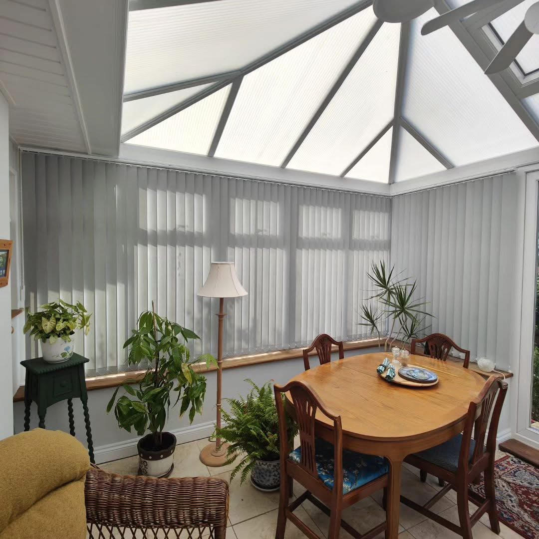Grey vertical blinds in a bright conservatory dining space