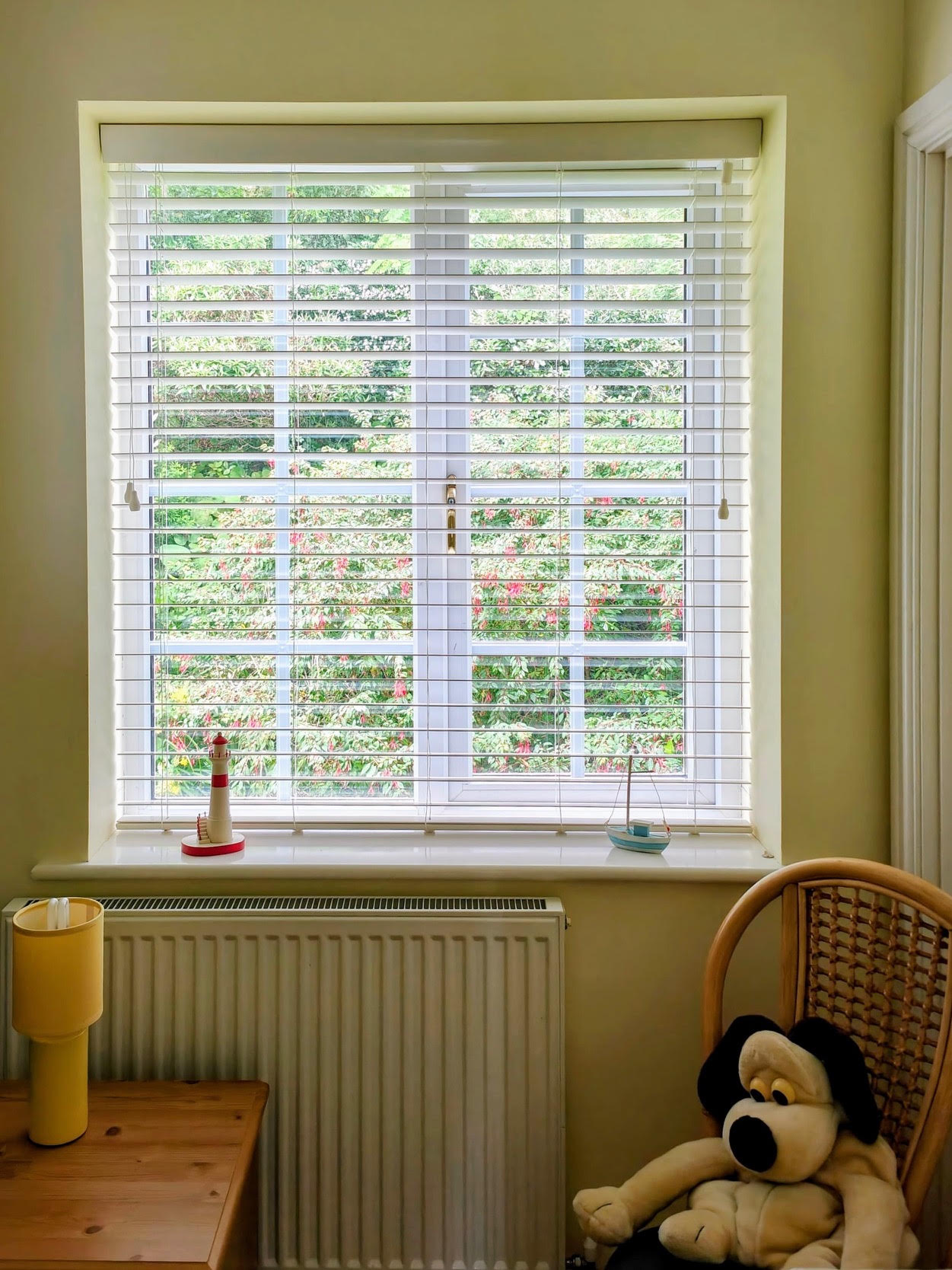 White wooden Venetian blind framing a lush garden view