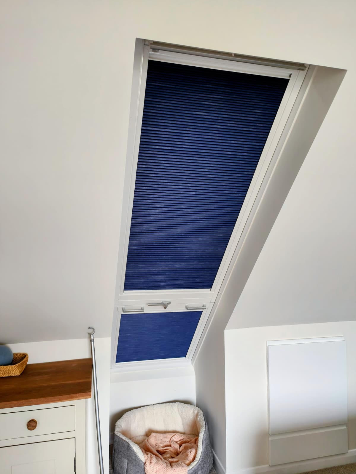 Blue pleated Velux blind fitted to a sloped roof window