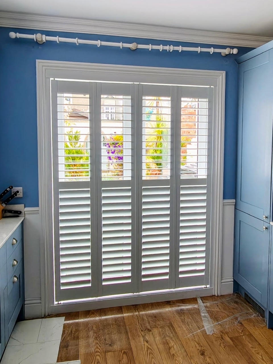 Grey tracked shutters in a blue kitchen with garden view