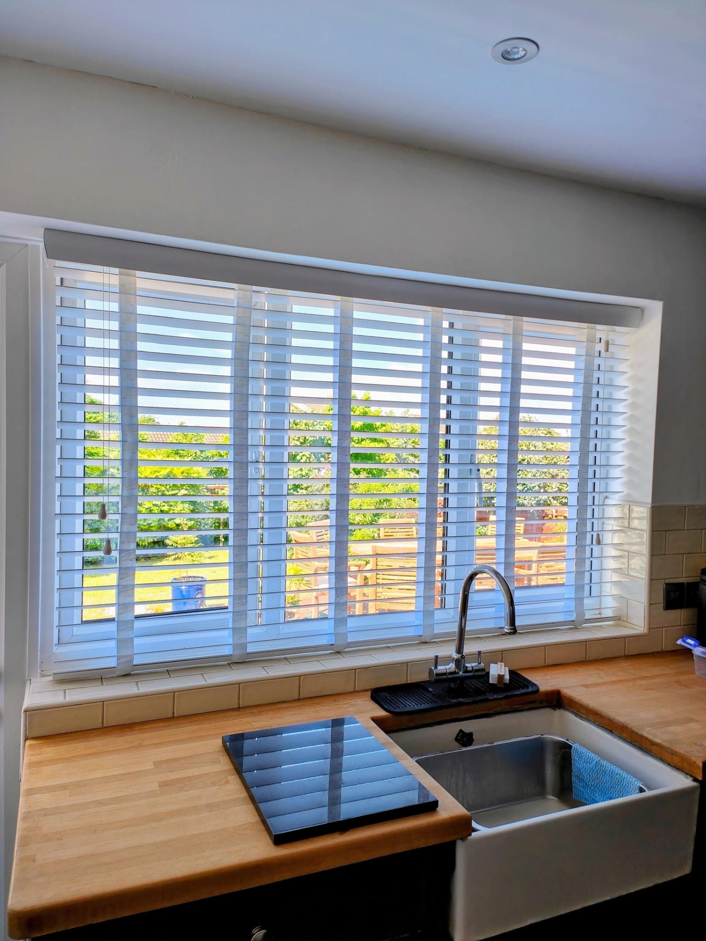 White wooden Venetian blinds across a wide kitchen window with garden view